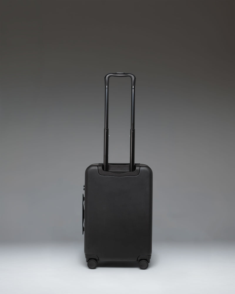 Black Herschel Heritage Hardshell Large CarryOn Luggage standing upright, showing its durable hardshell exterior, wheels, and retractable handle.