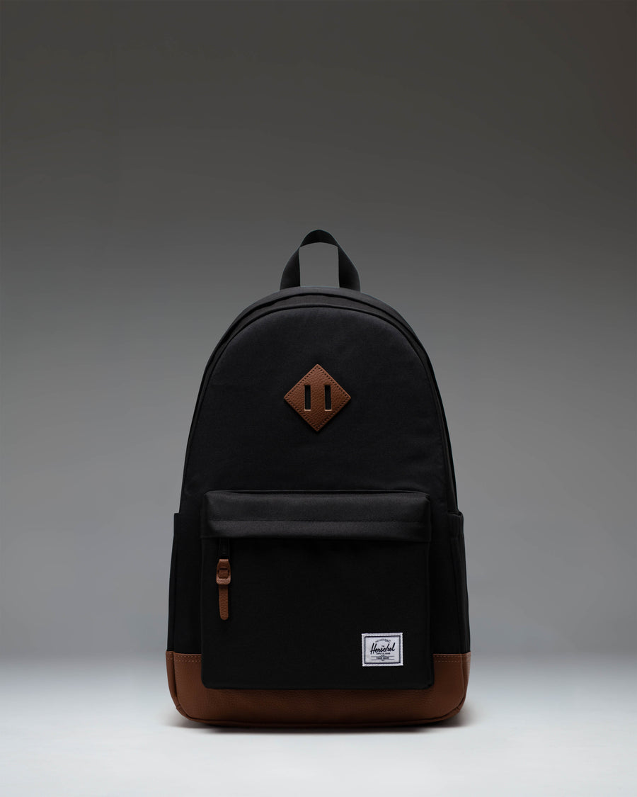 Herschel Heritage Backpack in Black with a Tan brown diamond accent and bottom panel, shown from the front on a white background.