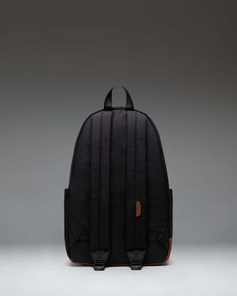 Herschel Heritage Backpack in Black/Tan shown from the side to highlight the profile, shoulder straps, and classic diamond accent.