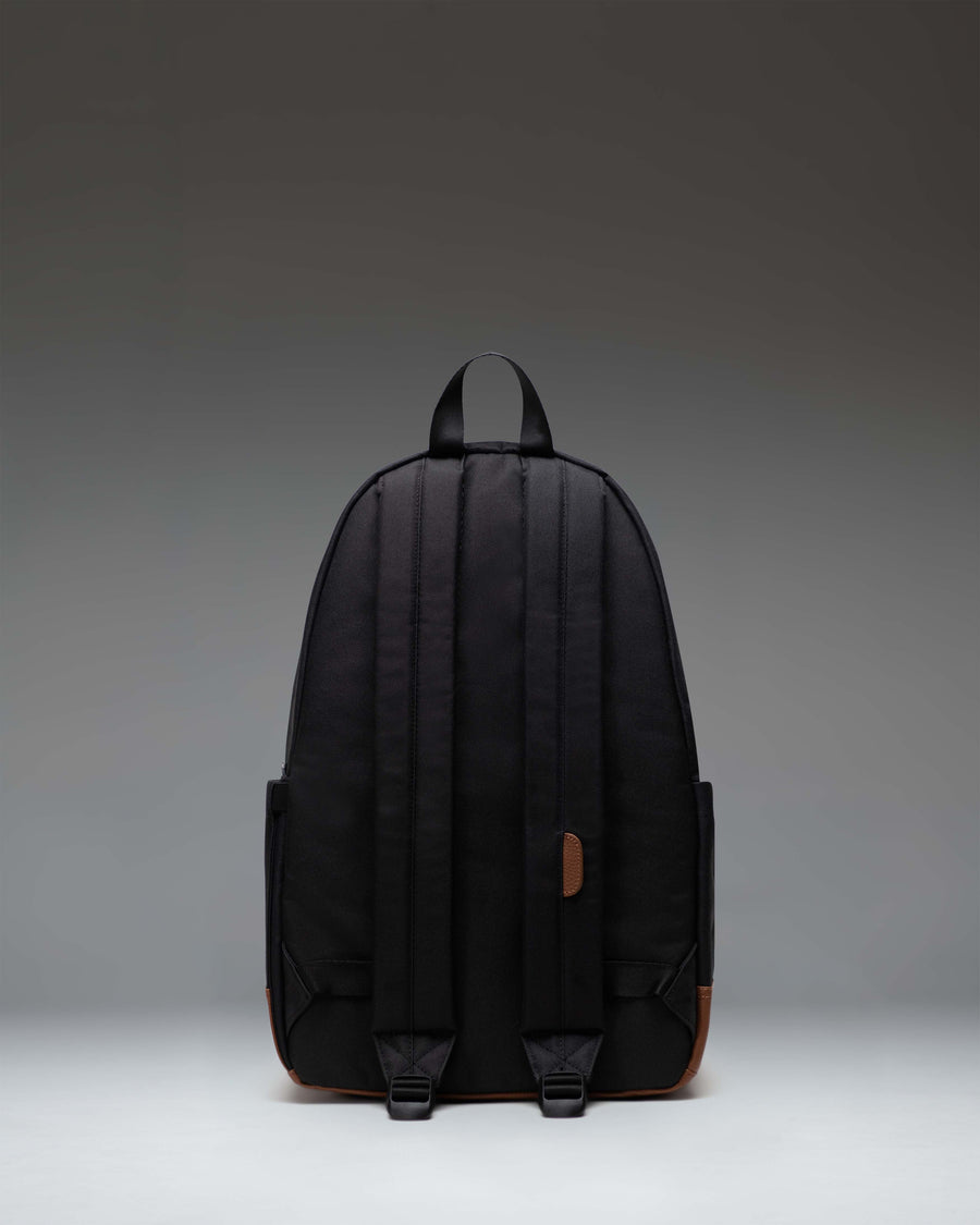 Herschel Heritage Backpack in Black/Tan shown from the side to highlight the profile, shoulder straps, and classic diamond accent.