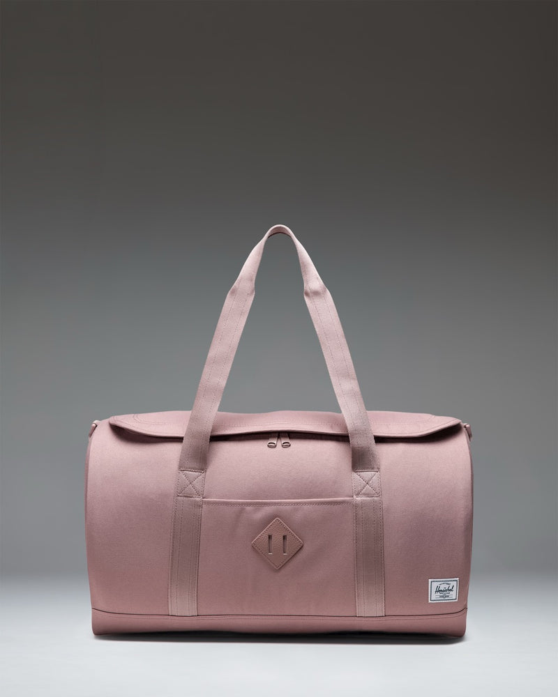 Herschel Supply Co. Heritage Duffle bag in Ash Rose pink, showing a clean side view with top handles and a shoulder strap.