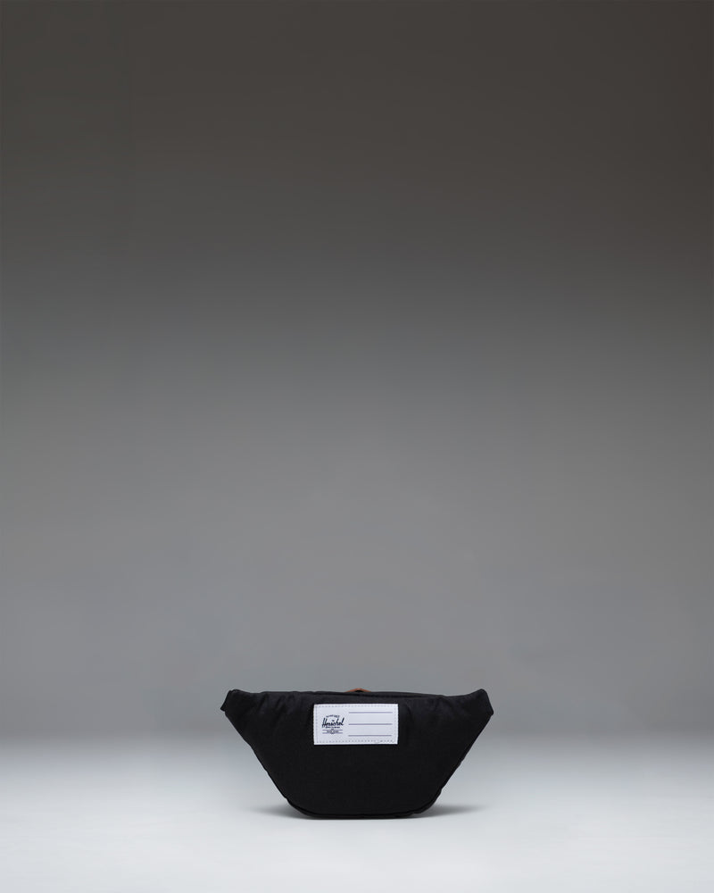 Black Little Herschel Heritage Hip Pack shown from the back, featuring an adjustable webbed strap with a plastic buckle clip.