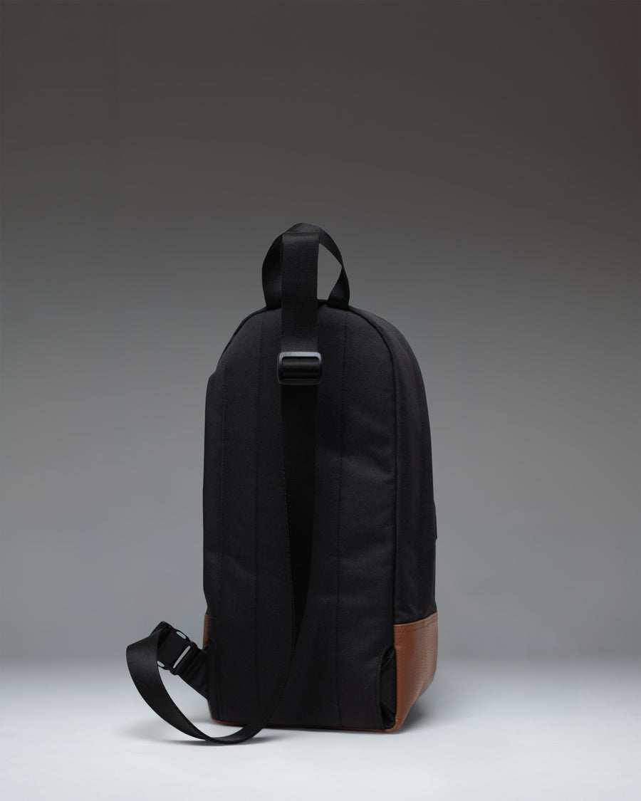 Black Herschel Heritage Shoulder Bag with a tan synthetic leather base, classic woven label, and an adjustable crossbody strap.