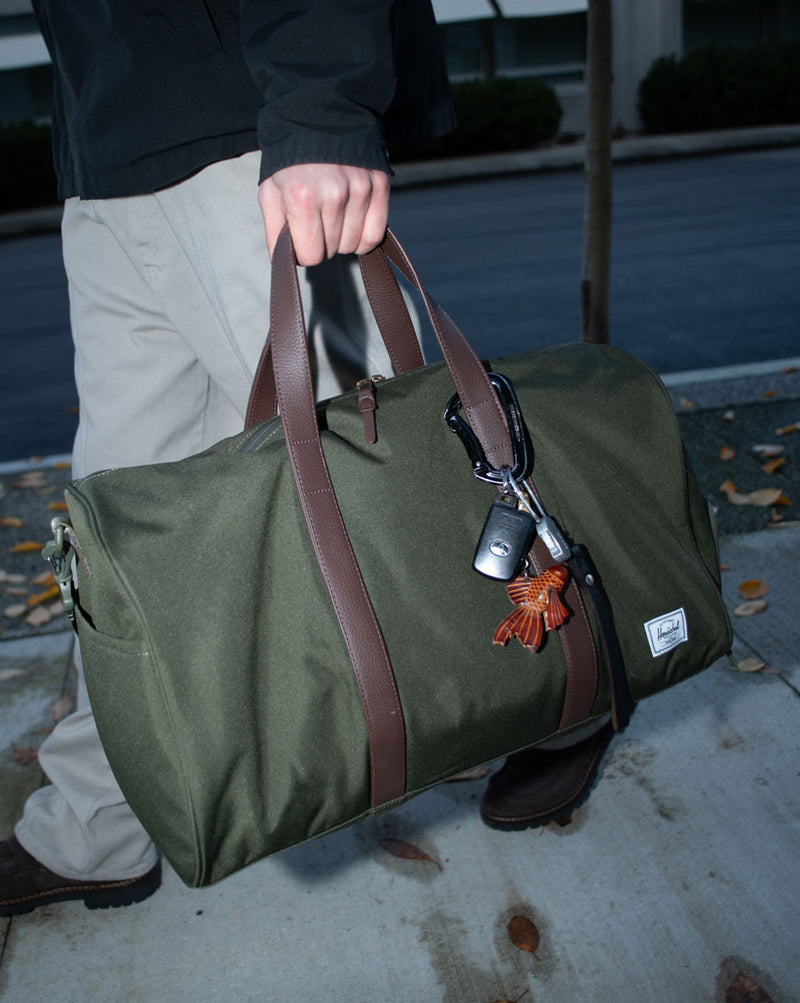 Herschel Supply Co. Novel Duffle size guide chart showing dimensions for Carry On (26.5L), Standard (43L), and Tech (45L) options.
