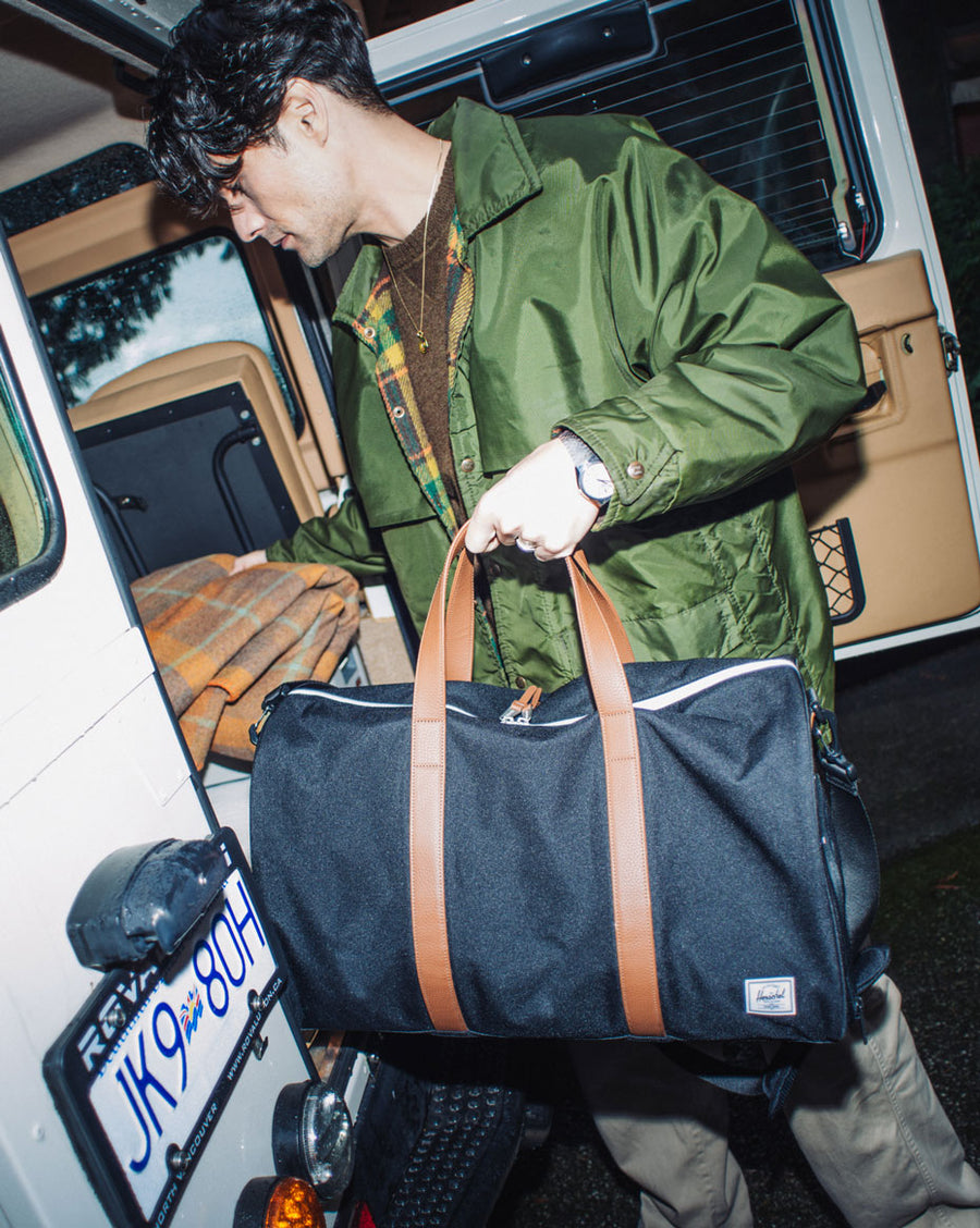 A collection of Herschel Supply Co. Novel Duffle bags arranged together in a variety of different colors and patterns.