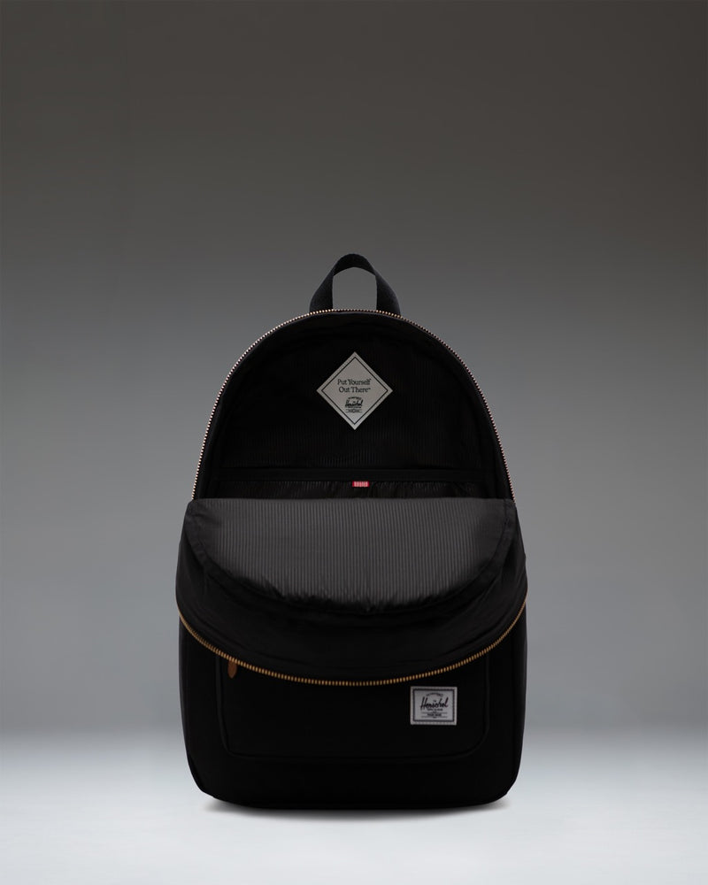 Classic black Herschel Supply Co. Settlement Backpack with exposed gold zippers, brown leather pulls, and a front storage pocket.