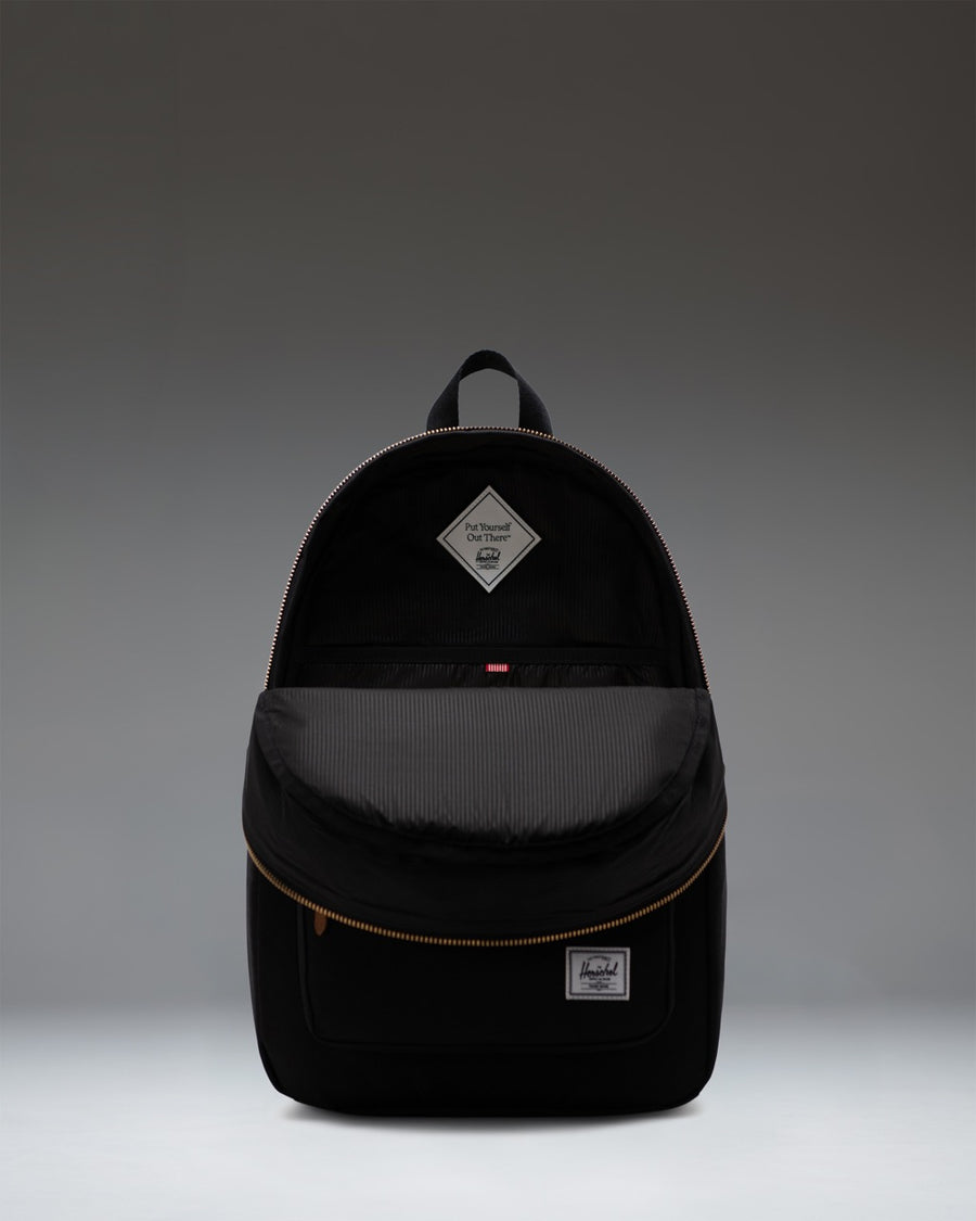 Classic black Herschel Supply Co. Settlement Backpack with exposed gold zippers, brown leather pulls, and a front storage pocket.