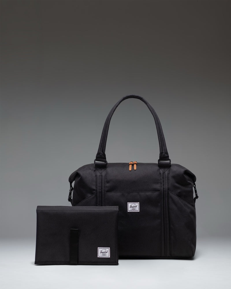 Herschel Supply Co. Strand Duffle Diaper Bag in black, featuring top handles, a removable shoulder strap, and front storage sleeves.