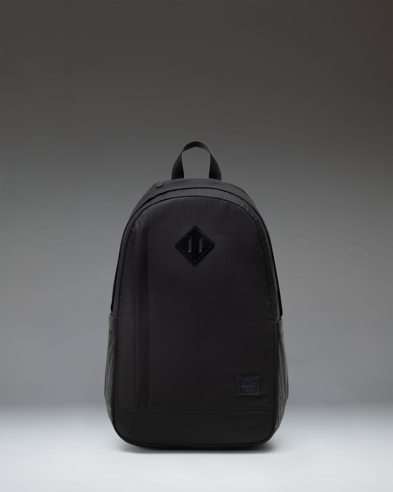 Herschel Seymour Backpack in black, showing the front view with dual straps, a front zippered pocket, and the classic Herschel woven label.