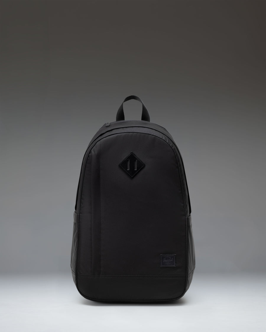 Herschel Seymour Backpack in black, showing the front view with dual straps, a front zippered pocket, and the classic Herschel woven label.