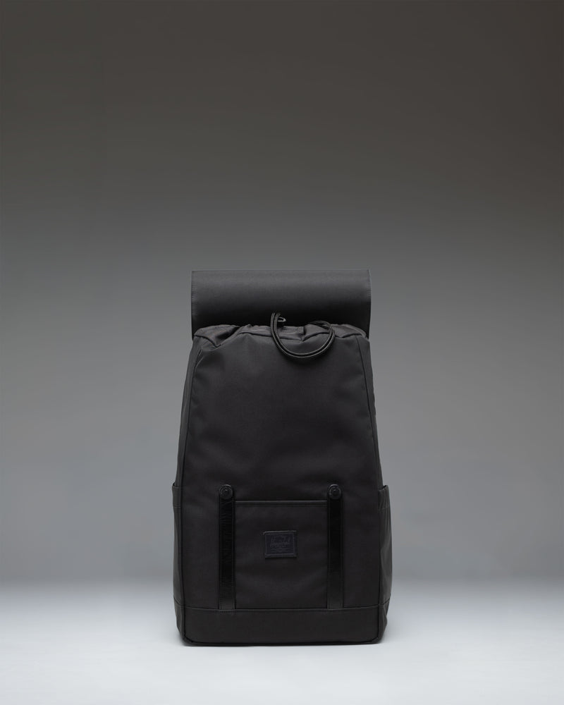 Herschel Retreat Small Backpack in black, featuring dual rubber straps with metal buckles and a classic woven label on the front pocket.