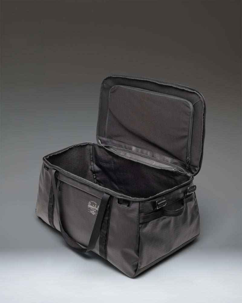 Black Herschel Supply Co. All Season Duffle Bag 66L shown from a three-quarter angle, highlighting its spacious design and durable material.
