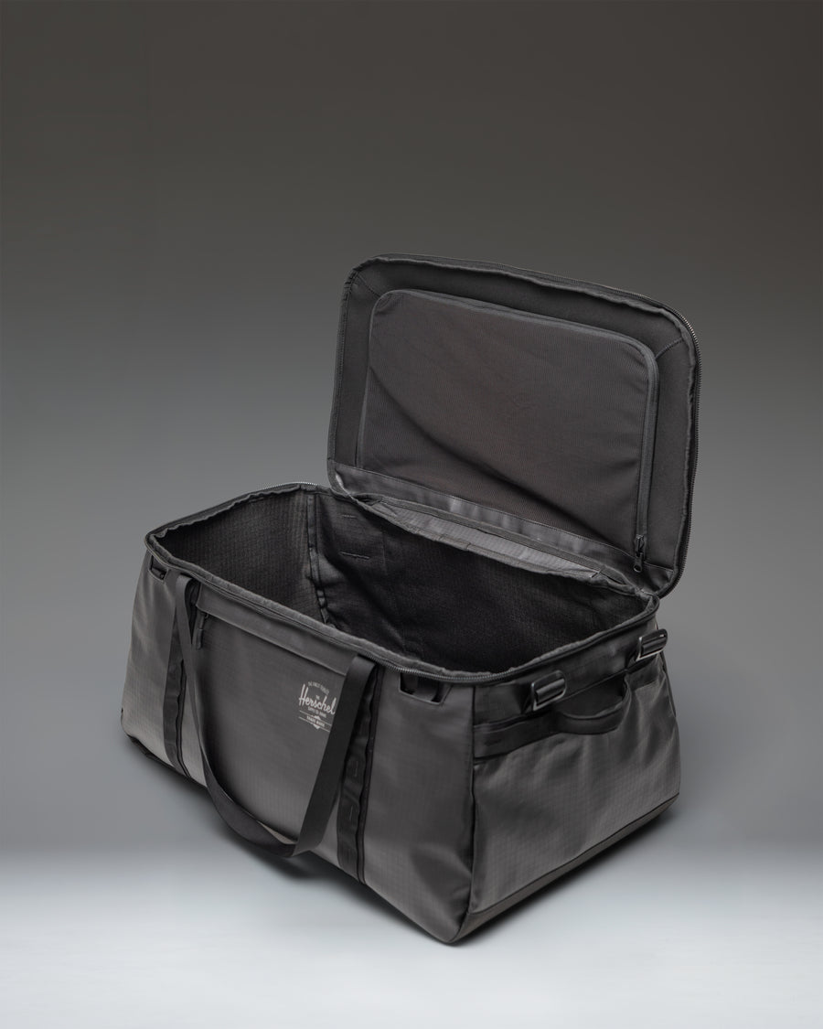 Black Herschel Supply Co. All Season Duffle Bag 66L shown from a three-quarter angle, highlighting its spacious design and durable material.