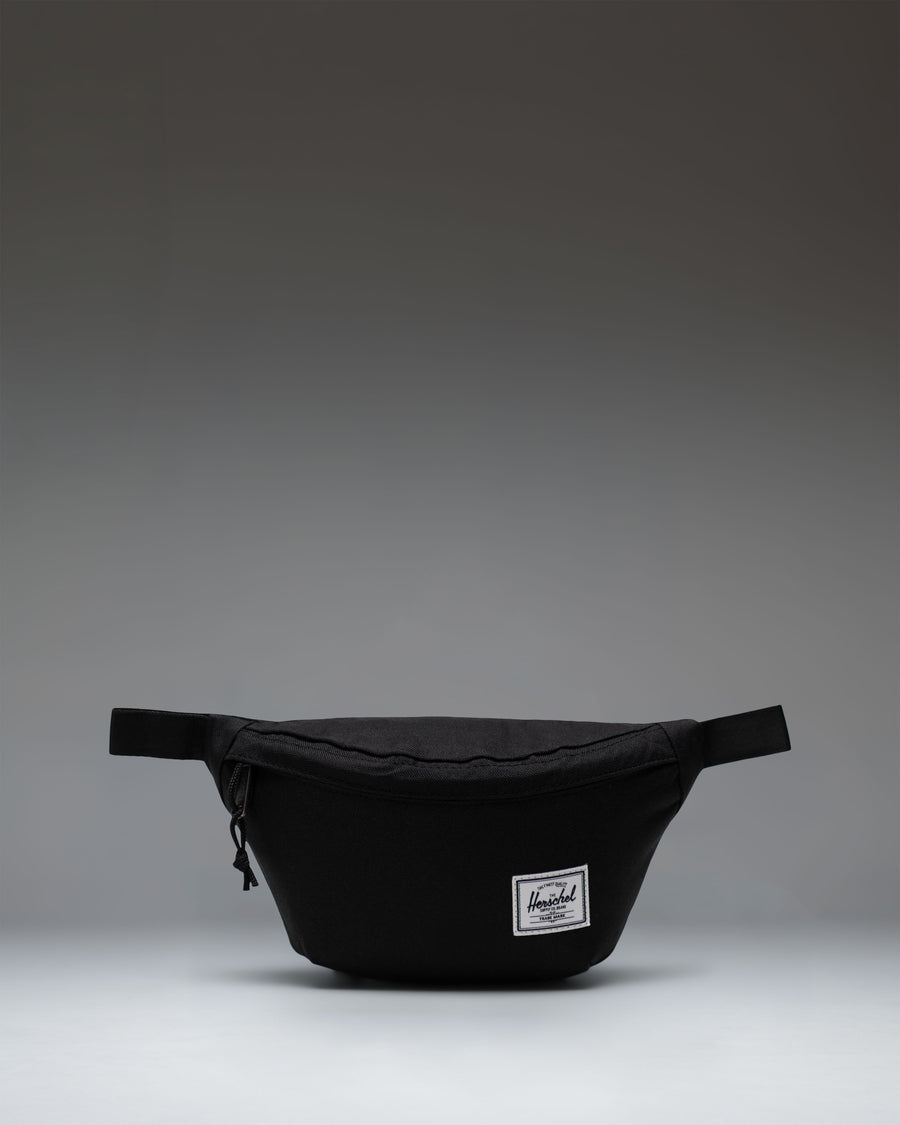 Black Herschel Classic Hip Pack featuring a main zippered compartment, front pocket, and adjustable webbed strap.