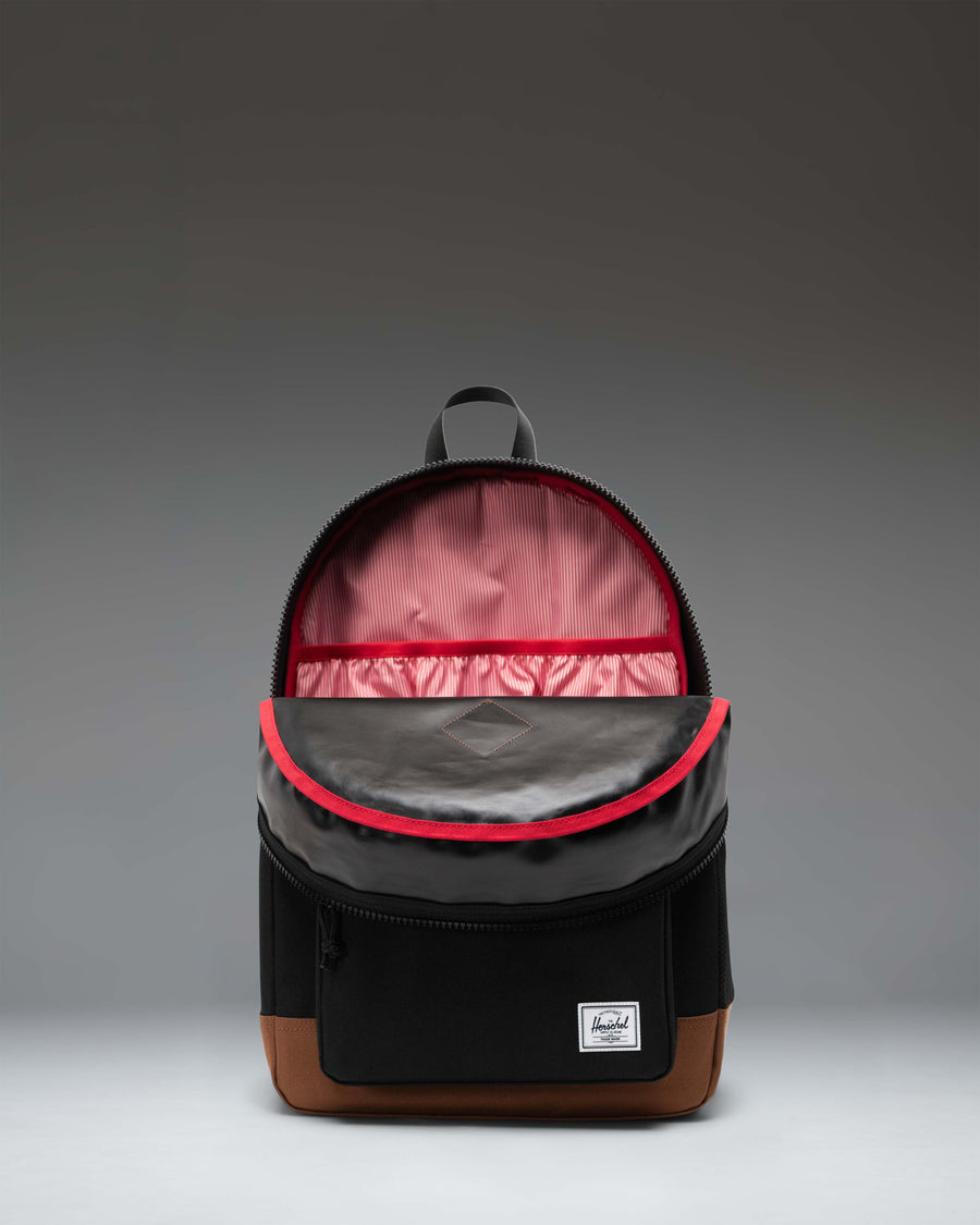 Herschel Heritage Youth Backpack in Black with a Saddle Brown bottom panel, featuring a front pocket and padded shoulder straps.