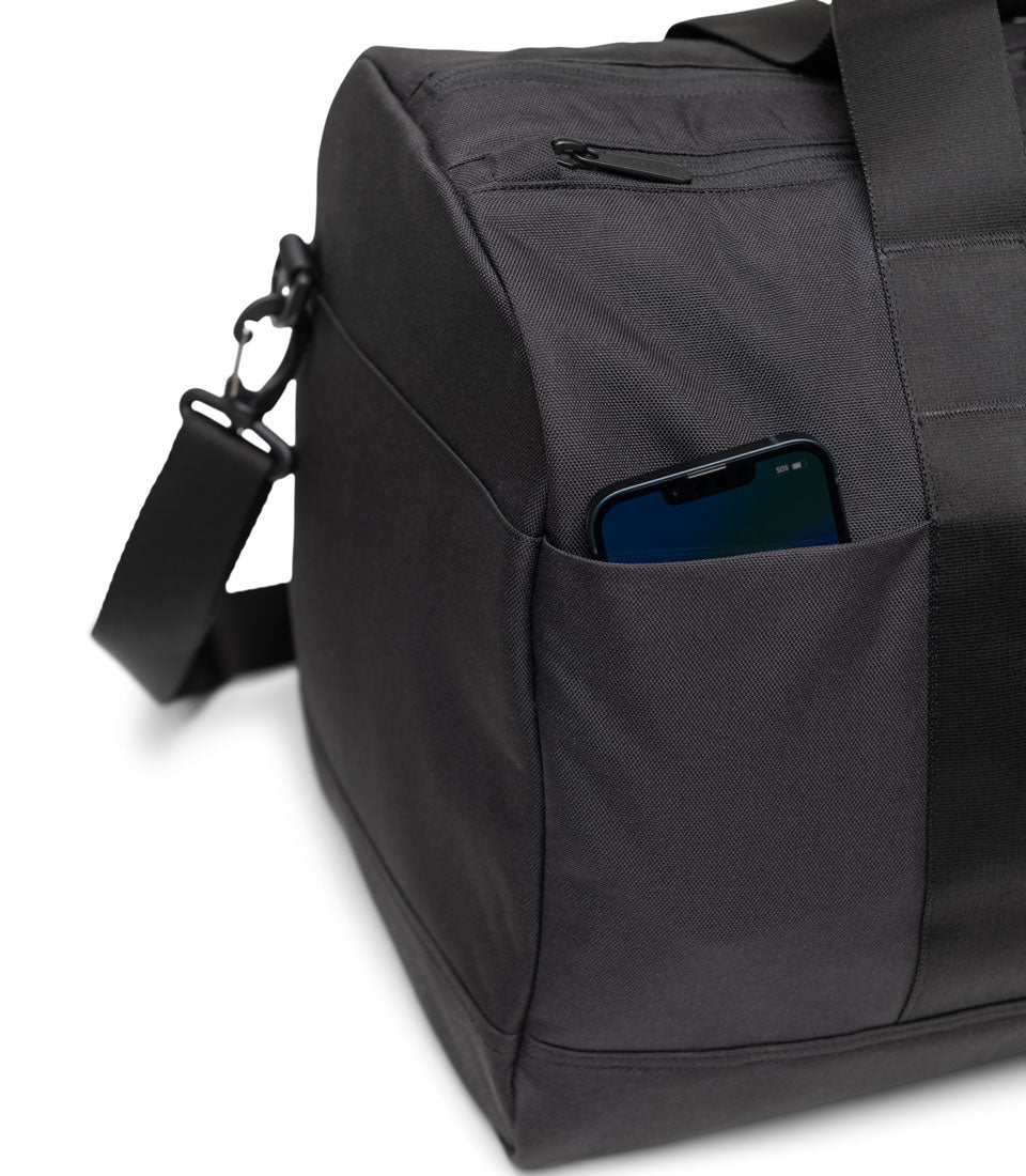 Herschel Supply Co. Novel Duffle Tech bag showcasing its smart luggage trolley sleeve feature by being stacked over the handle of a rolling suitcase.