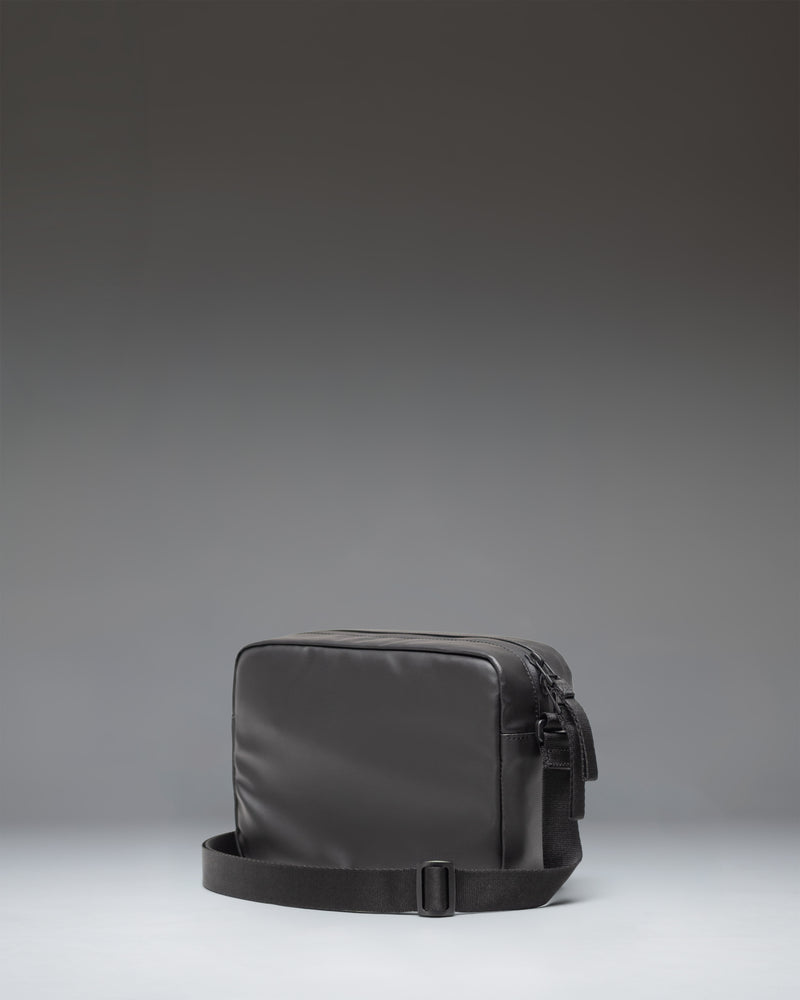 Herschel Supply Co. Alberni Crossbody bag in black, shown from the side to highlight its slim profile and adjustable shoulder strap.