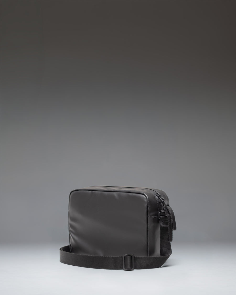 Herschel Supply Co. Alberni Crossbody bag in black, shown from the side to highlight its slim profile and adjustable shoulder strap.