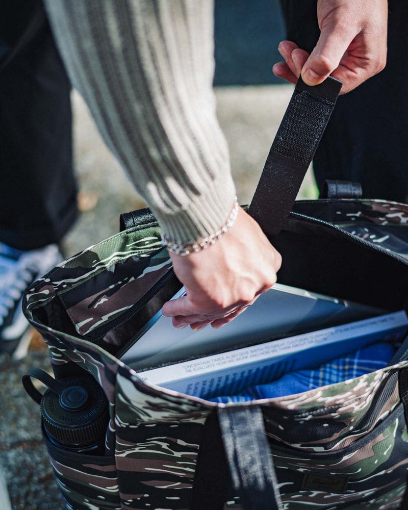 Herschel Supply Co. x Realtree limited-edition collection essential bags, apparel, and accessories arranged together in the APX camouflage pattern.