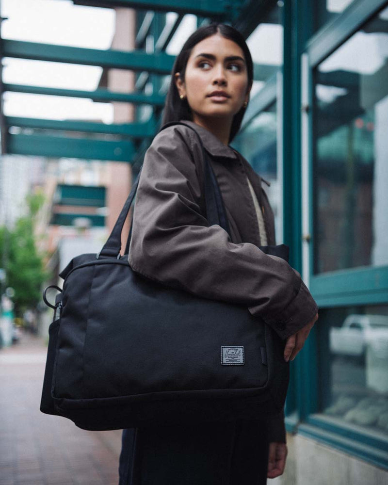 Herschel Supply Co. Kaslo Tote Tech Cordura 23L black tote bag displayed showing its multi-compartment design, laptop sleeve, and luggage sleeve.