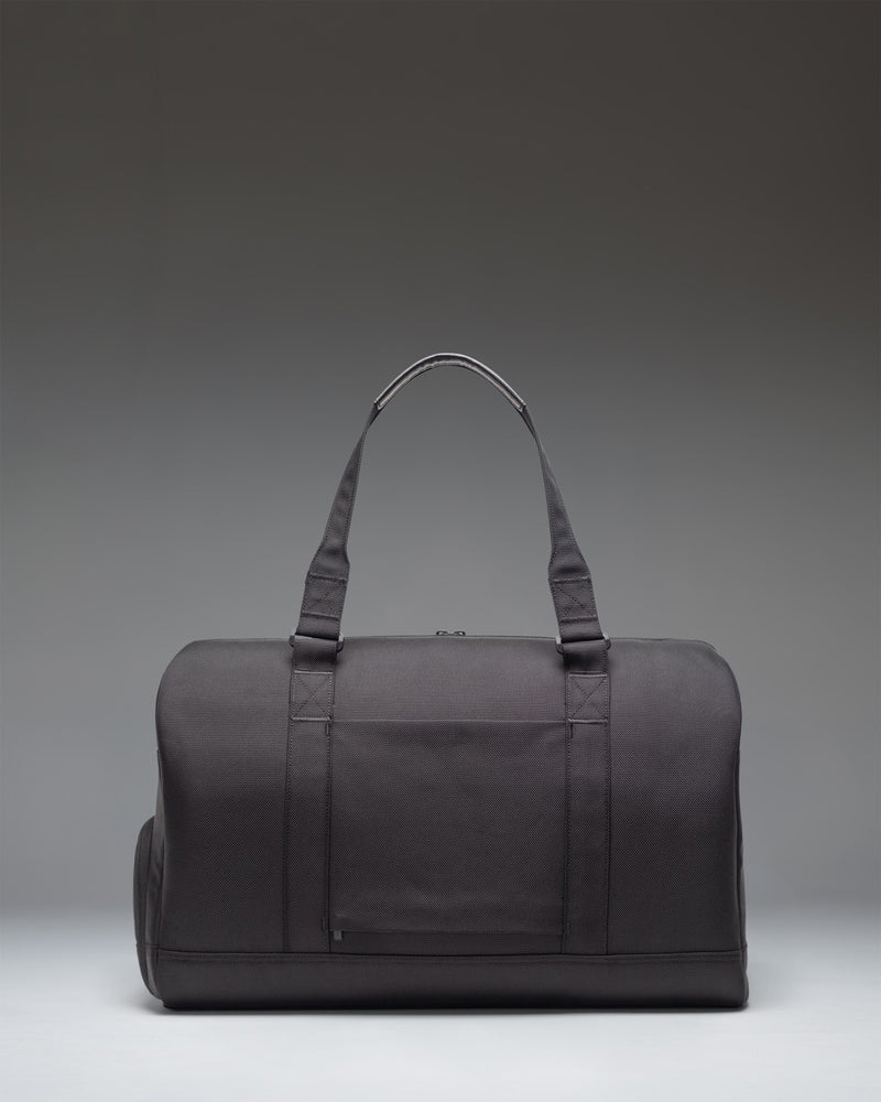 Herschel Novel Duffle Tech Cordura in black, featuring a side profile view highlighting the durable fabric, carrying handles, and shoulder strap.