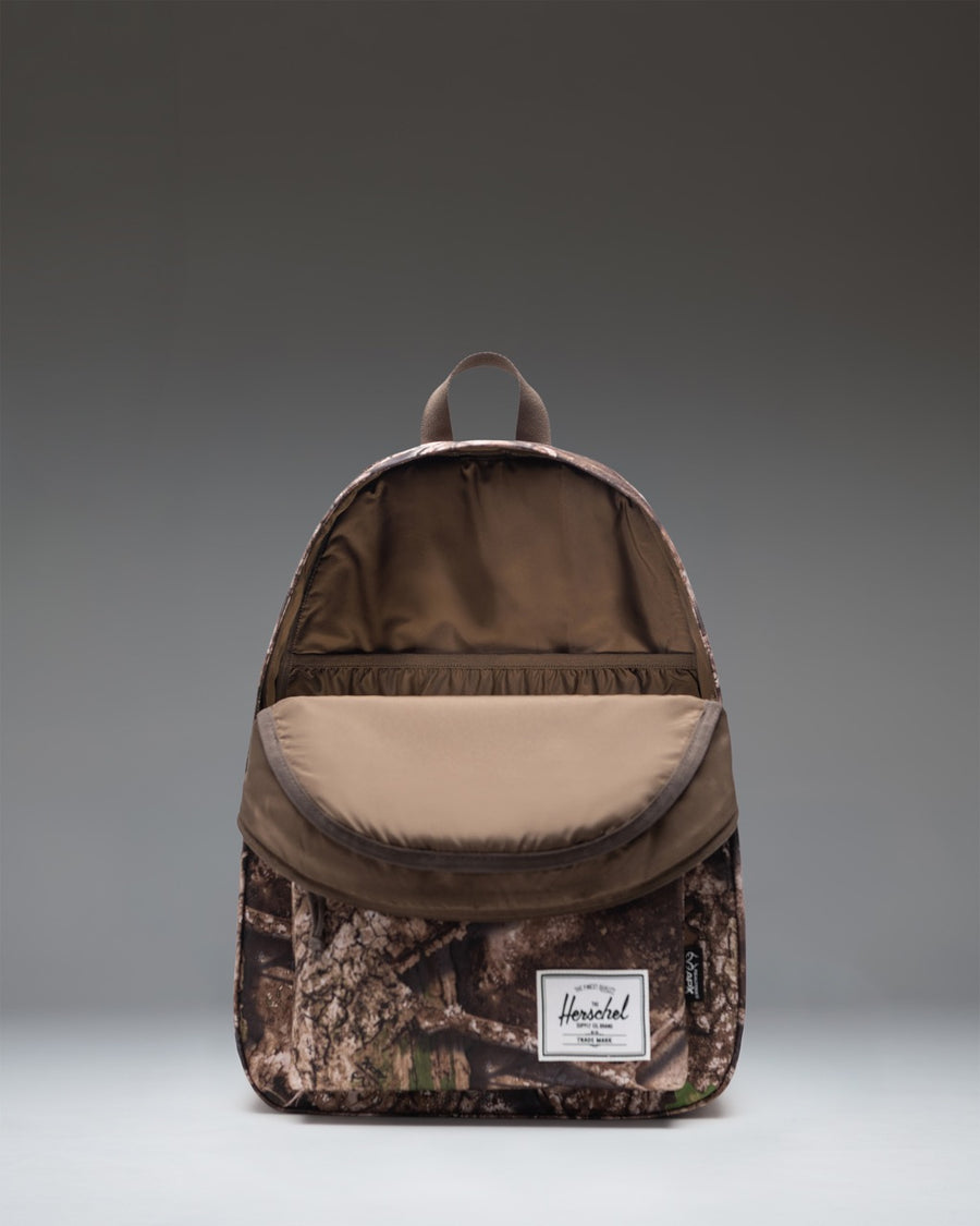 Herschel Supply Co. Classic XL Backpack in Realtree APX Camo, showcasing the front pocket, main compartment, and signature woven label.