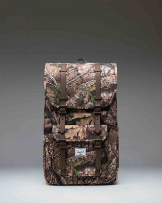 Herschel Little America Backpack in Realtree APX Camo featuring black straps and a front pocket.