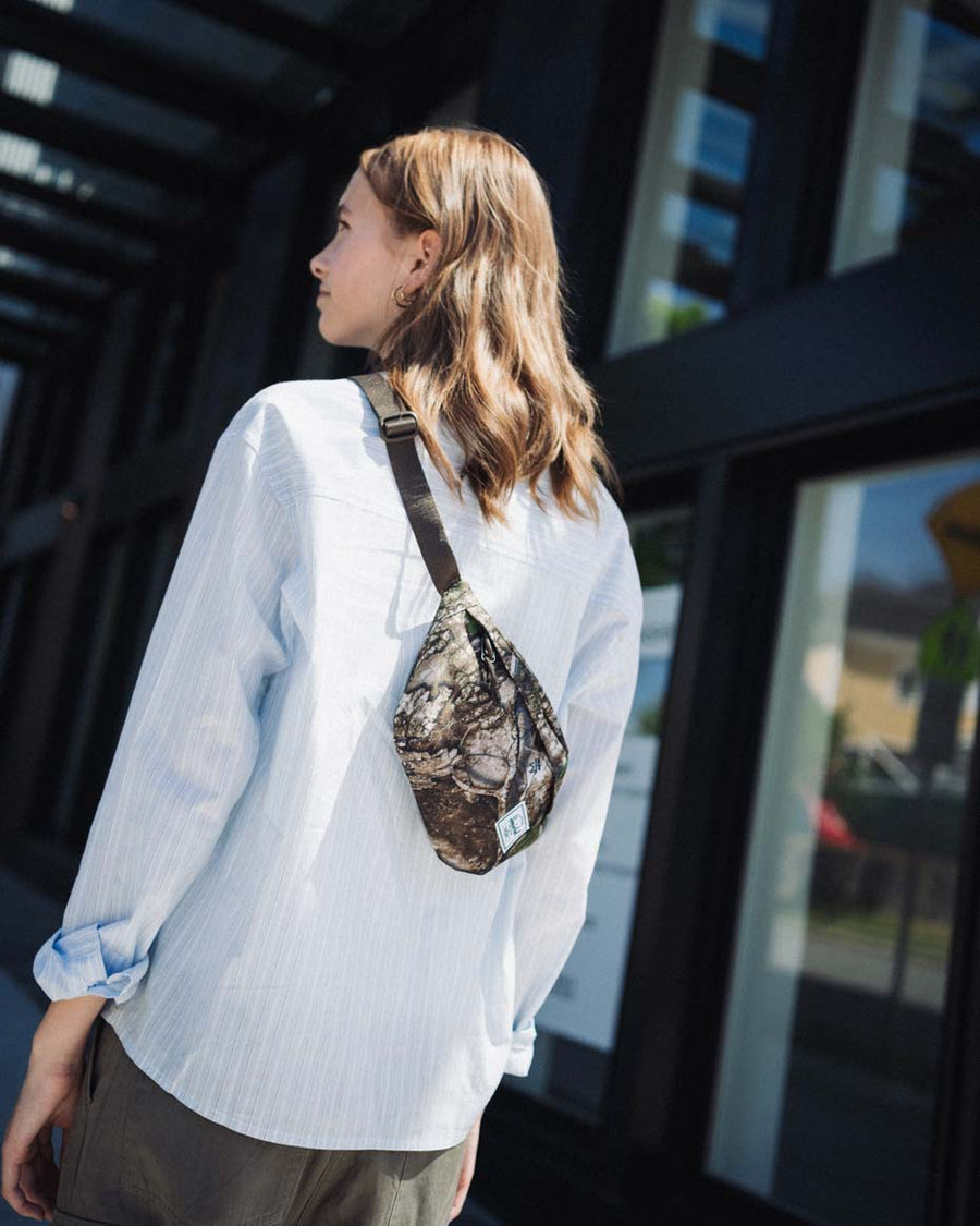 Herschel Classic hip pack in Realtree APX camo pattern. Compact design with zippered closure and adjustable webbing strap.