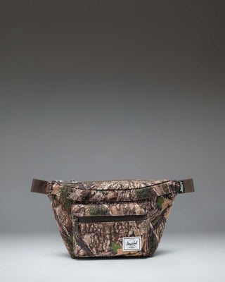 Herschel Supply Co. Pop Quiz Hip Pack in Realtree APX Camo pattern, showing the adjustable strap and front zipper pocket.