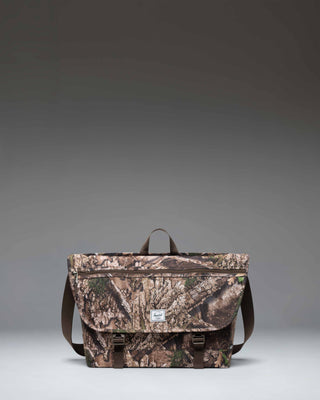 Herschel Supply Co. Realtree Cove Messenger bag in Realtree APX Camo pattern, showing the front design with straps and buckles.
