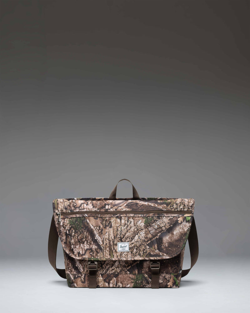Herschel Supply Co. Realtree Cove Messenger bag in Realtree APX Camo pattern, showing the front design with straps and buckles.