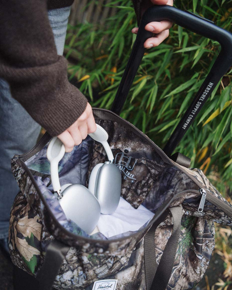 Herschel Supply Co. x Realtree limited-edition collection essential bags, apparel, and accessories arranged together in the APX camouflage pattern.