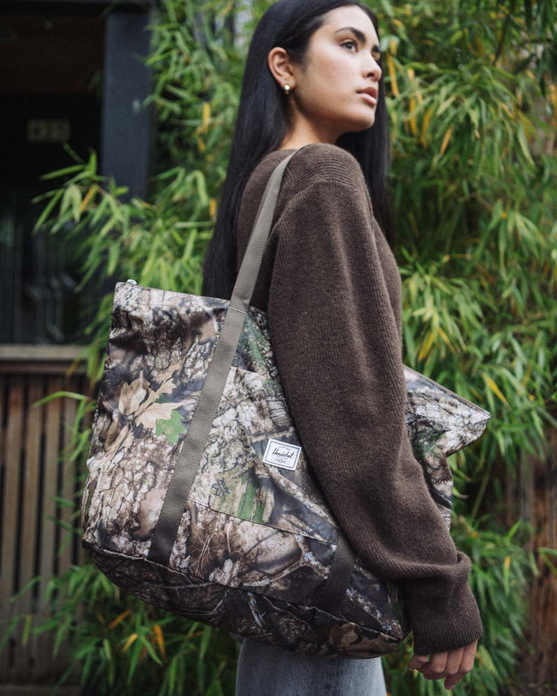 Herschel Supply Co. x Realtree limited-edition collection essential bags, apparel, and accessories arranged together in the APX camouflage pattern.