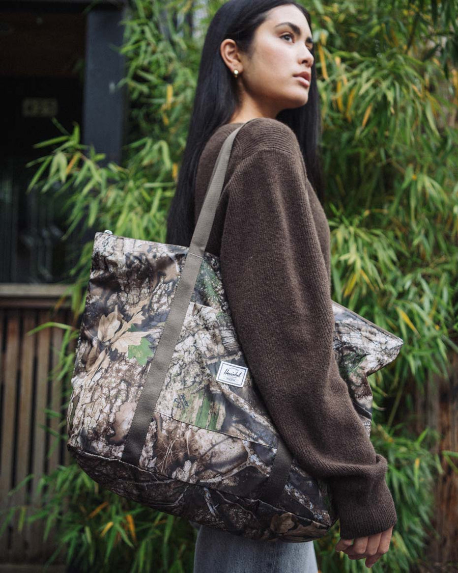 Herschel Supply Co. x Realtree limited-edition collection essential bags, apparel, and accessories arranged together in the APX camouflage pattern.