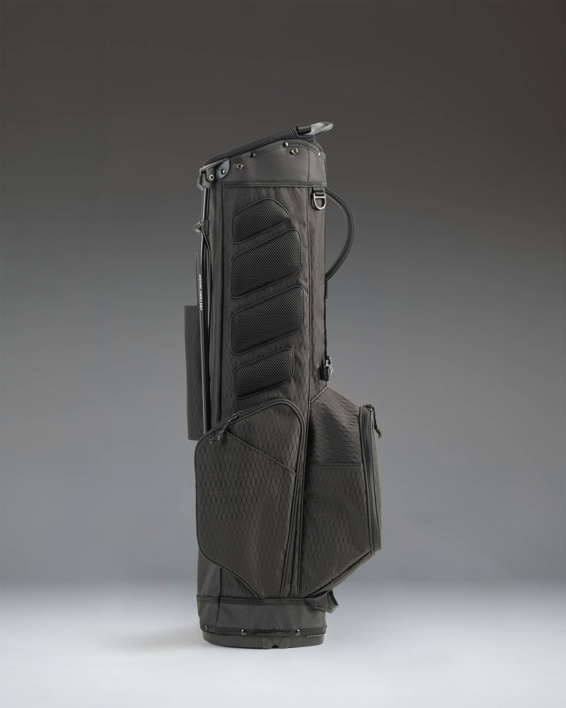 Herschel Watt Light Stand Bag in sleek black, showing a side view of the golf bag with its sturdy stand legs extended and dividers visible.