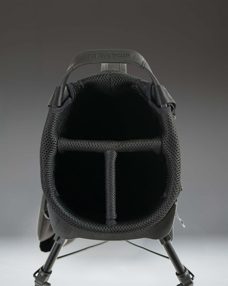 Herschel Watt Light Stand Bag in Black, showcasing a lifestyle view of the golf bag standing on a course.