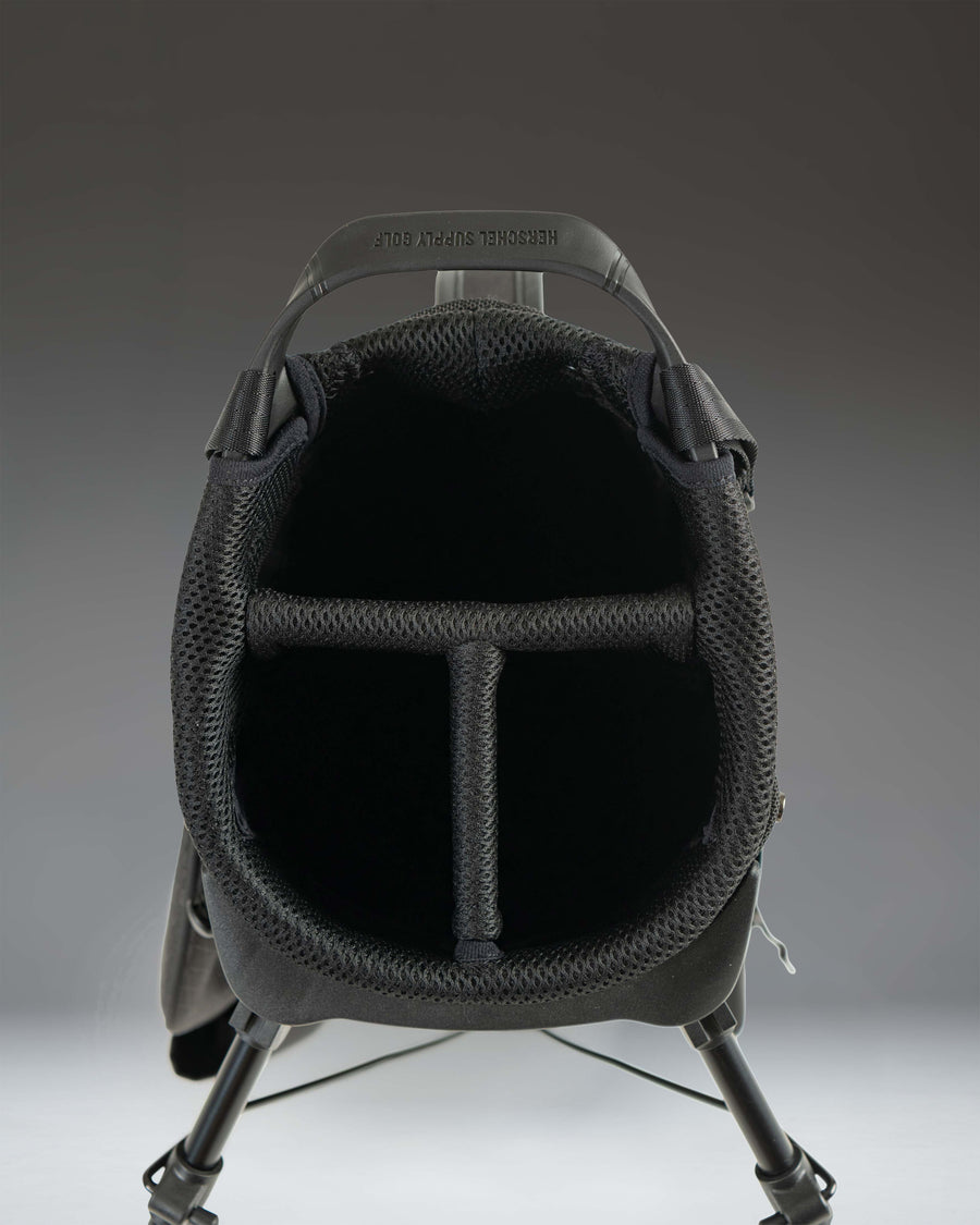 Herschel Watt Light Stand Bag in Black, showcasing a lifestyle view of the golf bag standing on a course.