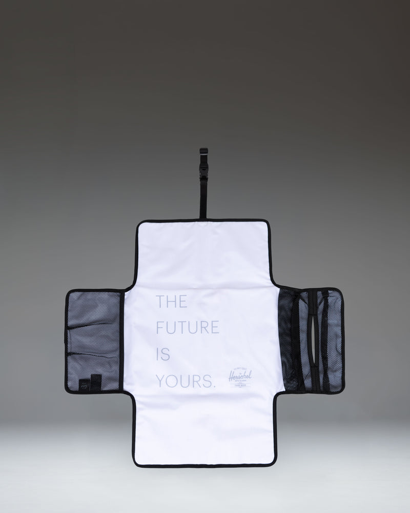 Herschel Supply Co. Sprout Change Mat in black, unfolded to show the padded mesh surface and internal mesh storage pockets.