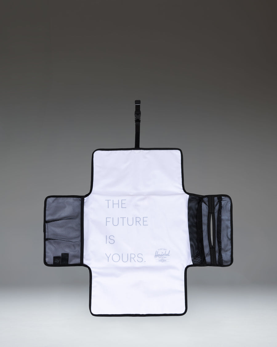 Herschel Supply Co. Sprout Change Mat in black, unfolded to show the padded mesh surface and internal mesh storage pockets.
