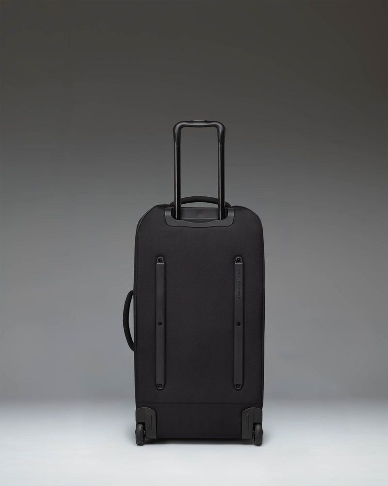 Black Herschel Heritage Softshell Medium Luggage being pulled by a person, showing the side view and wheels.