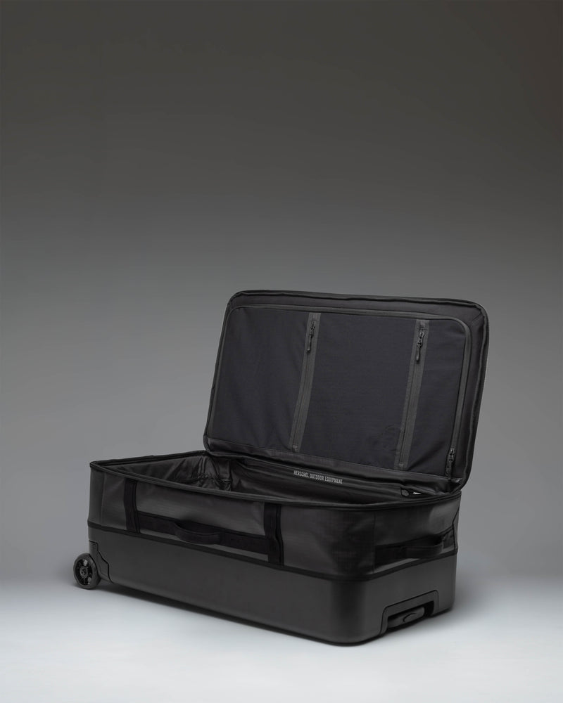 Herschel Supply Co. All Season Hybrid Roller Bag Large in black, showing the front exterior view with wheels and retractable handle.