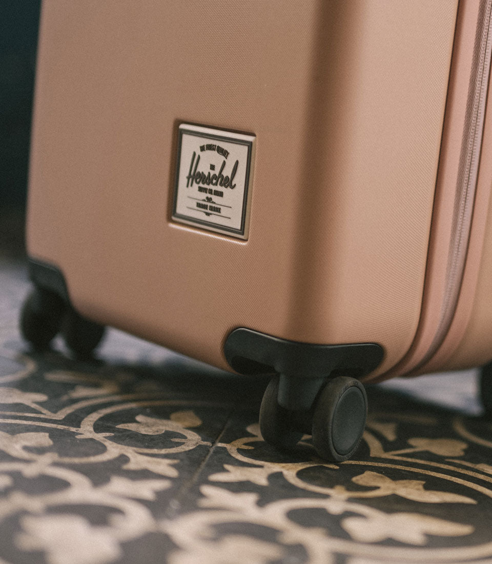 Herschel Heritage Hardshell Large Carry-On Luggage in Ash Rose showing features like durable split design, quiet Hinomoto wheels, and a TSA-approved lock.