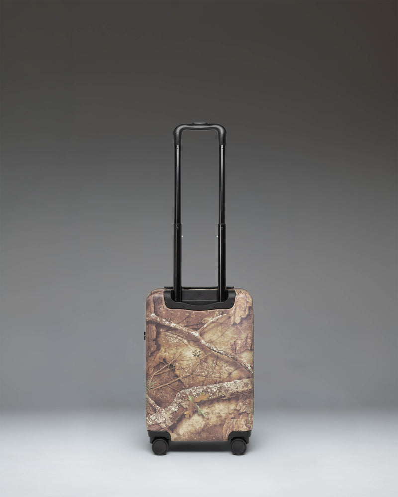 Herschel Supply Co. Herschel Heritage Carry On Luggage in Realtree APX Camo, showing the side view with black handles and wheels.