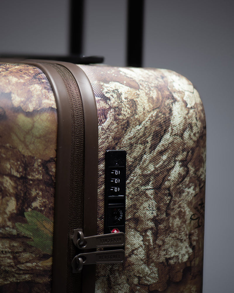 Herschel Supply Co. Realtree Heritage Carry On Luggage in Realtree APX Camo pattern, featuring a multi-directional four-wheel design.