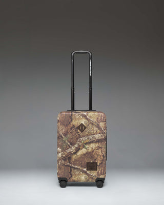 Herschel Heritage Large Carry-On Luggage in Realtree APX Camo pattern, showing the front view of the hard-shell suitcase.