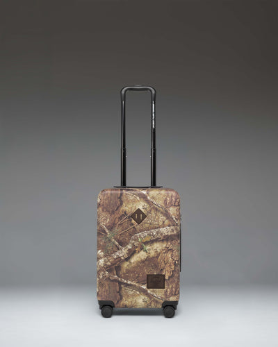 Herschel Heritage Large Carry-On Luggage in Realtree APX Camo pattern, showing the front view of the hard-shell suitcase.