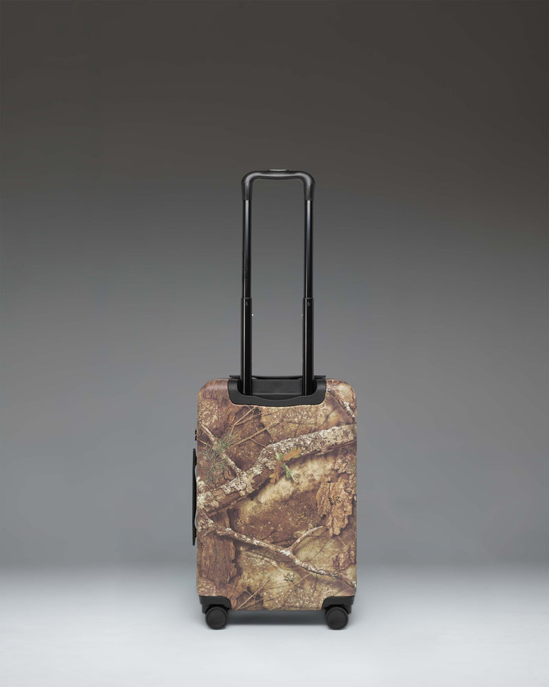 Herschel Supply Co. Herschel Heritage Large carry-on luggage in Realtree APX camo print, showing the side view with handles and wheels.