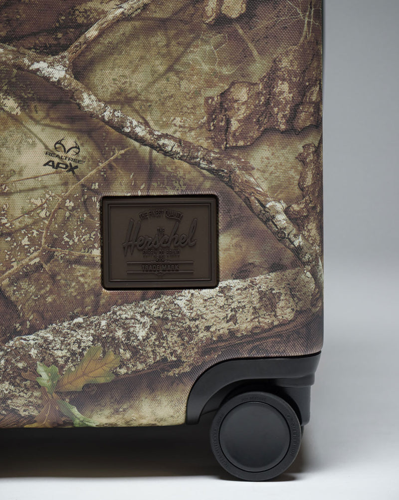 Herschel Supply Co. Realtree Heritage Medium Luggage in Realtree APX Camo pattern, showing a front view of the rolling suitcase.