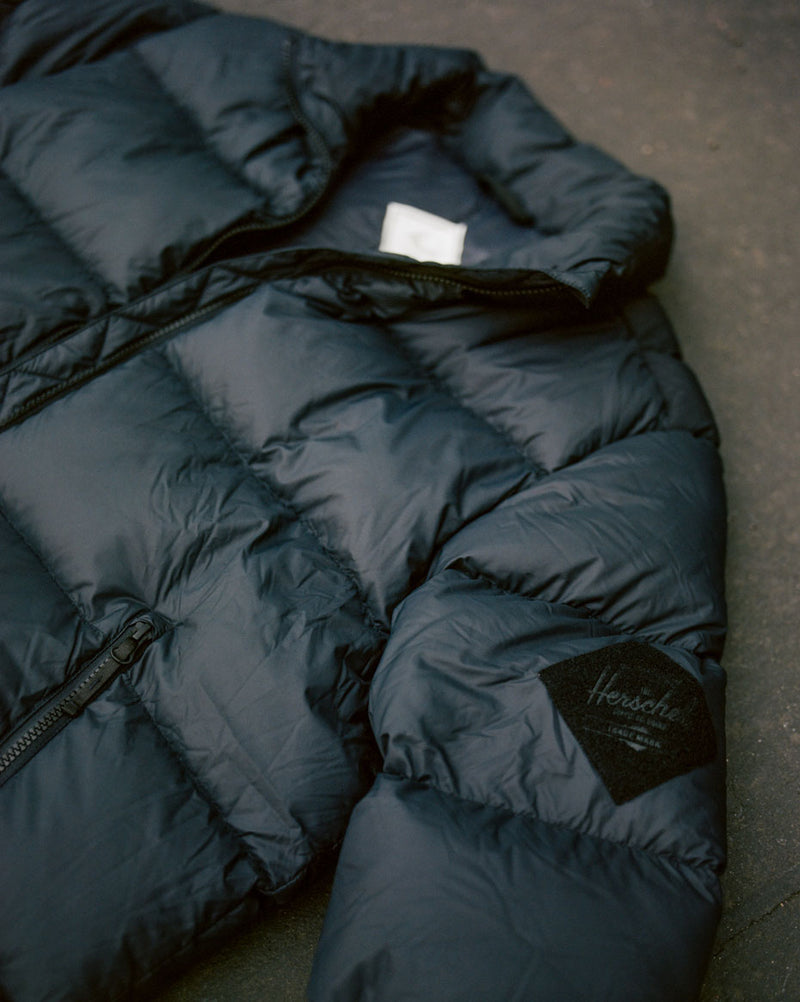 Herschel Supply Co. Men's Puffer Jacket in black, featuring a size guide chart with measurements for sizes XS through XXL.