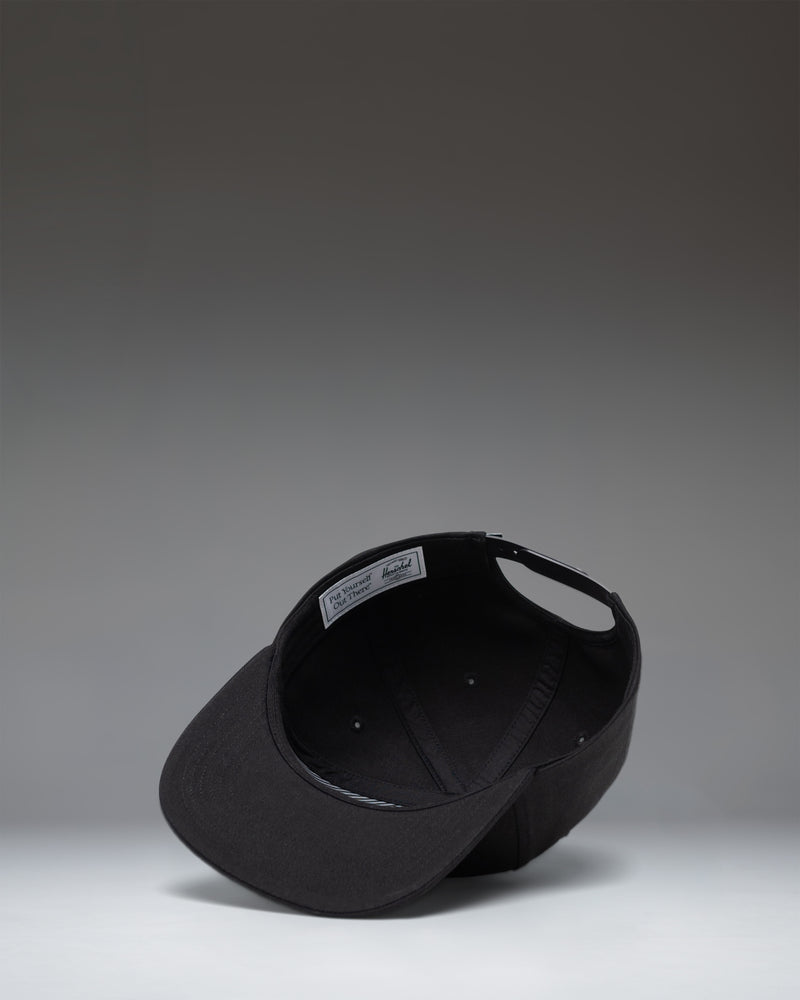 Herschel Supply Co Whaler 6 Panel Cap in black, featuring a structured crown, flat brim, and an adjustable strapback closure.